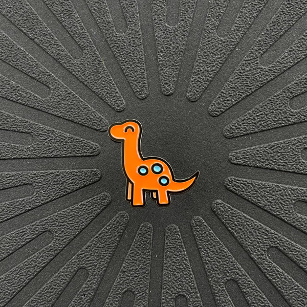 a single pinsnickety orange brontosaurus horse show number pin on a black background